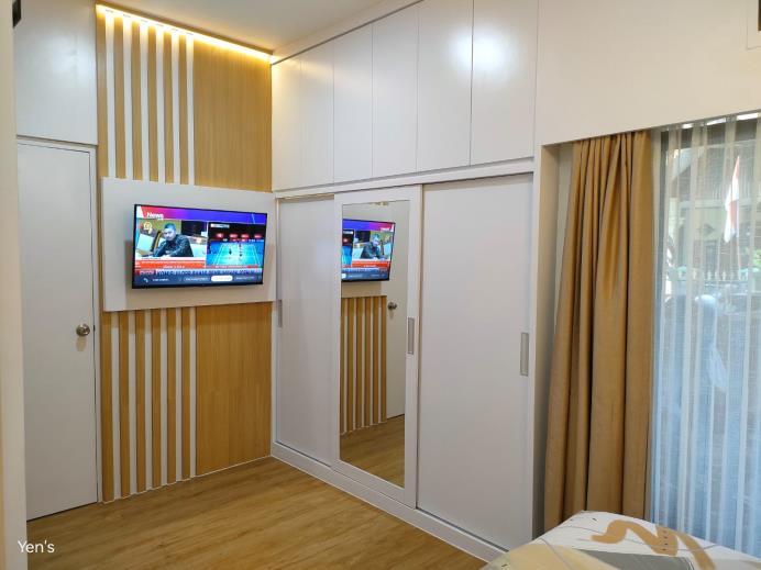 Interior kamar dengan panel TV, lemari putih, dan aksen kayu Yen Yen